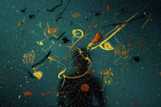 Abstract art of splattered paint in yellow, orange, and black on a dark blue background
