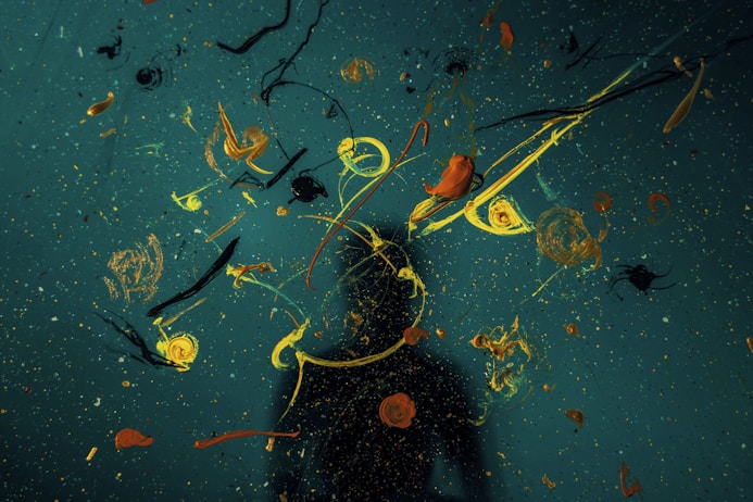 Abstract art of splattered paint in yellow, orange, and black on a dark blue background