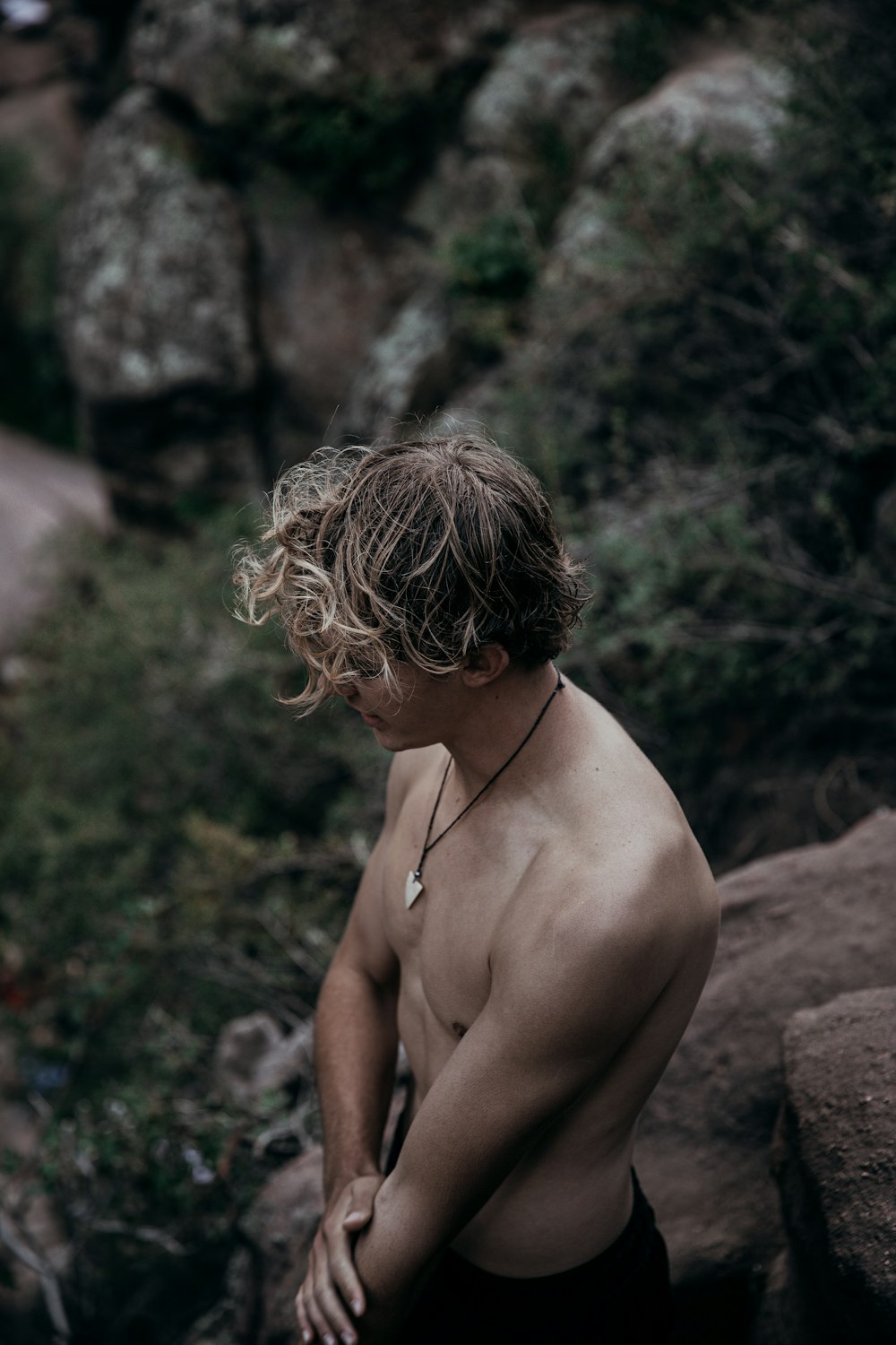 topless man sitting on rock during daytime