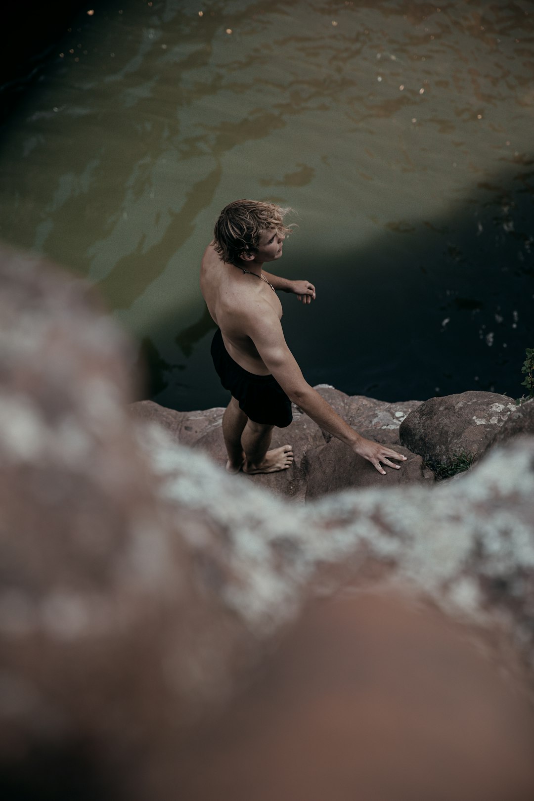 man in black shorts sitting on rock in water