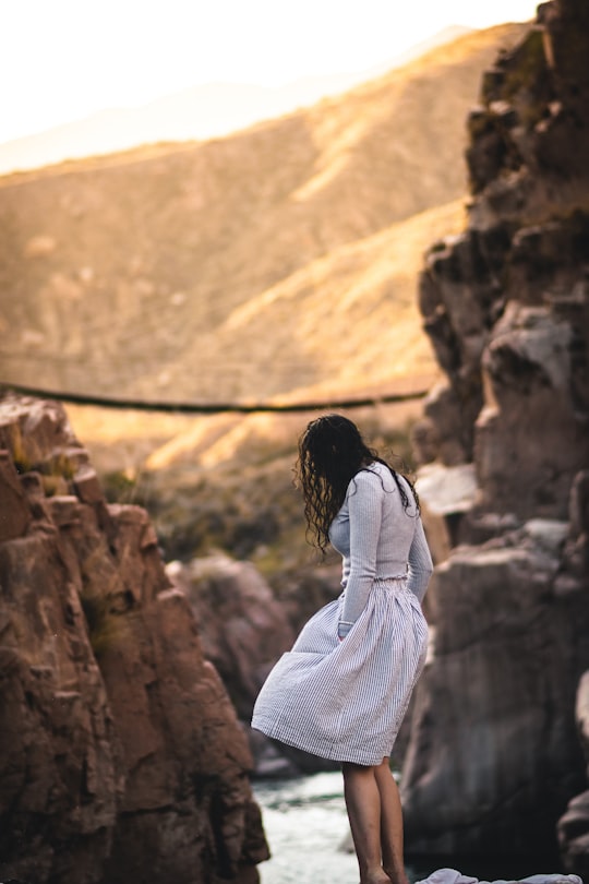 woman in white and black striped long sleeve shirt standing on brown rock formation during daytime in Mendoza Argentina