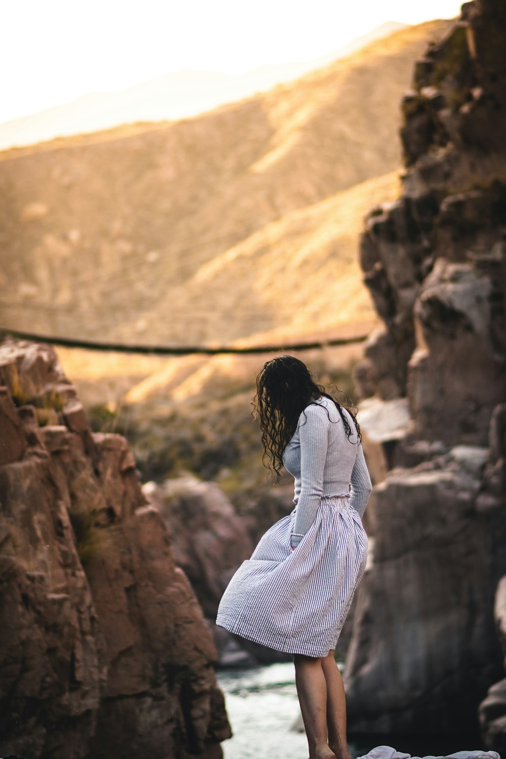 白と黒の縞模様の長袖シャツを着た女性が昼間、茶色の岩の上に立っている