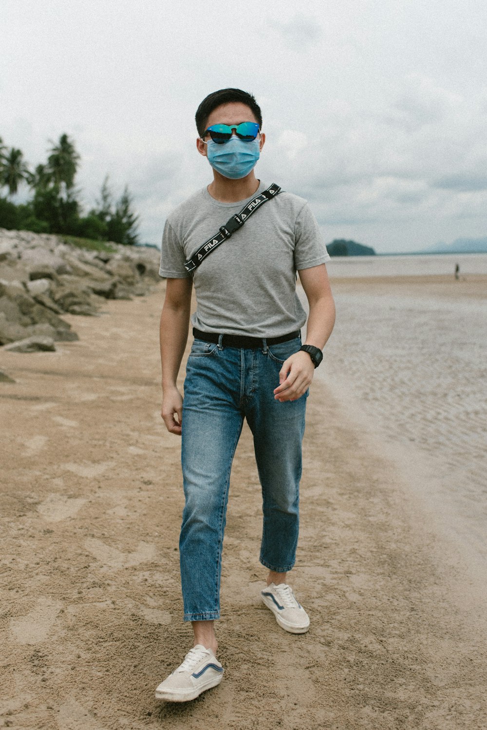 man in gray crew neck t-shirt and blue denim jeans standing on beach shore during
