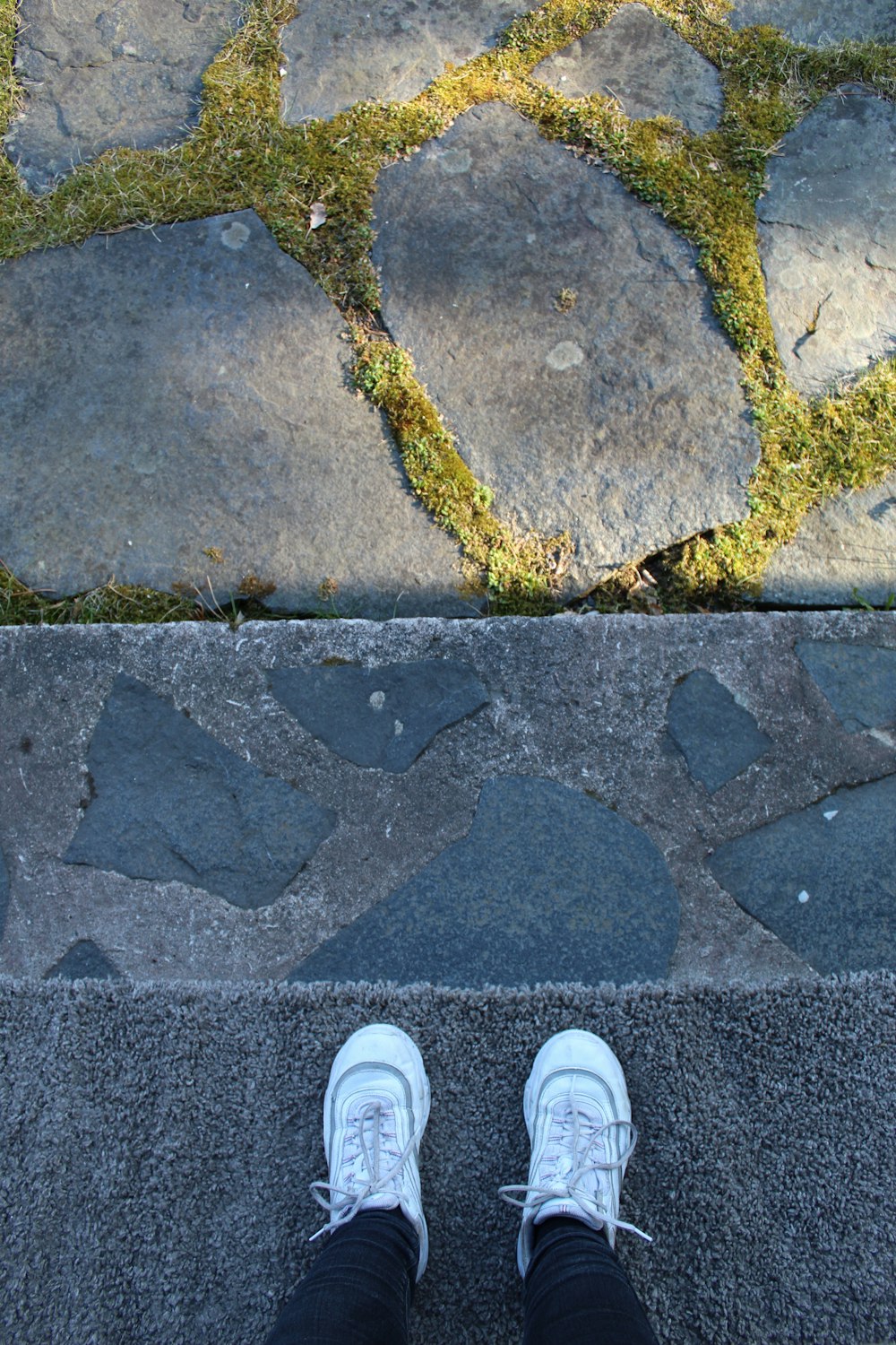 person in white sneakers standing on gray concrete pavement