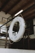 A lifebuoy is hanging from a rope in an indoor setting with wooden beams and glass panels. The text 'SAUVETEURS EN MER GF SN SM' is visible on the lifebuoy. The background includes framed pictures and dark furniture.