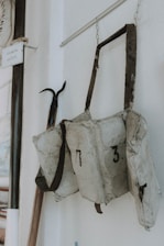Three worn, numbered flotation devices or life jackets hang on a wall, marked with a black number seven and three. They are attached to a strap which is looped over a metallic hook. The background is plain, with some additional items partially visible, including a sign with text.