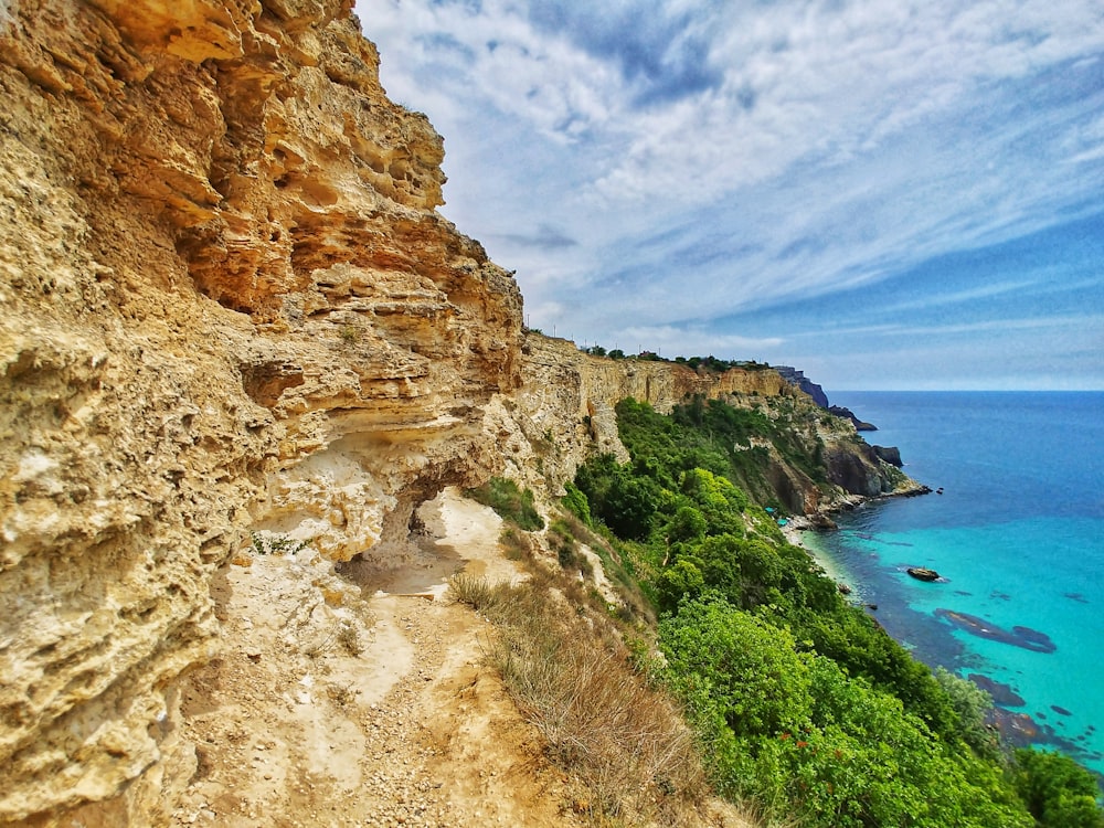 brown rocky mountain beside blue sea under blue sky during daytime