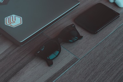 A sleek SLNT Faraday bag resting on a wooden desk beside a locked laptop and a smartphone, bathed in soft natural light.