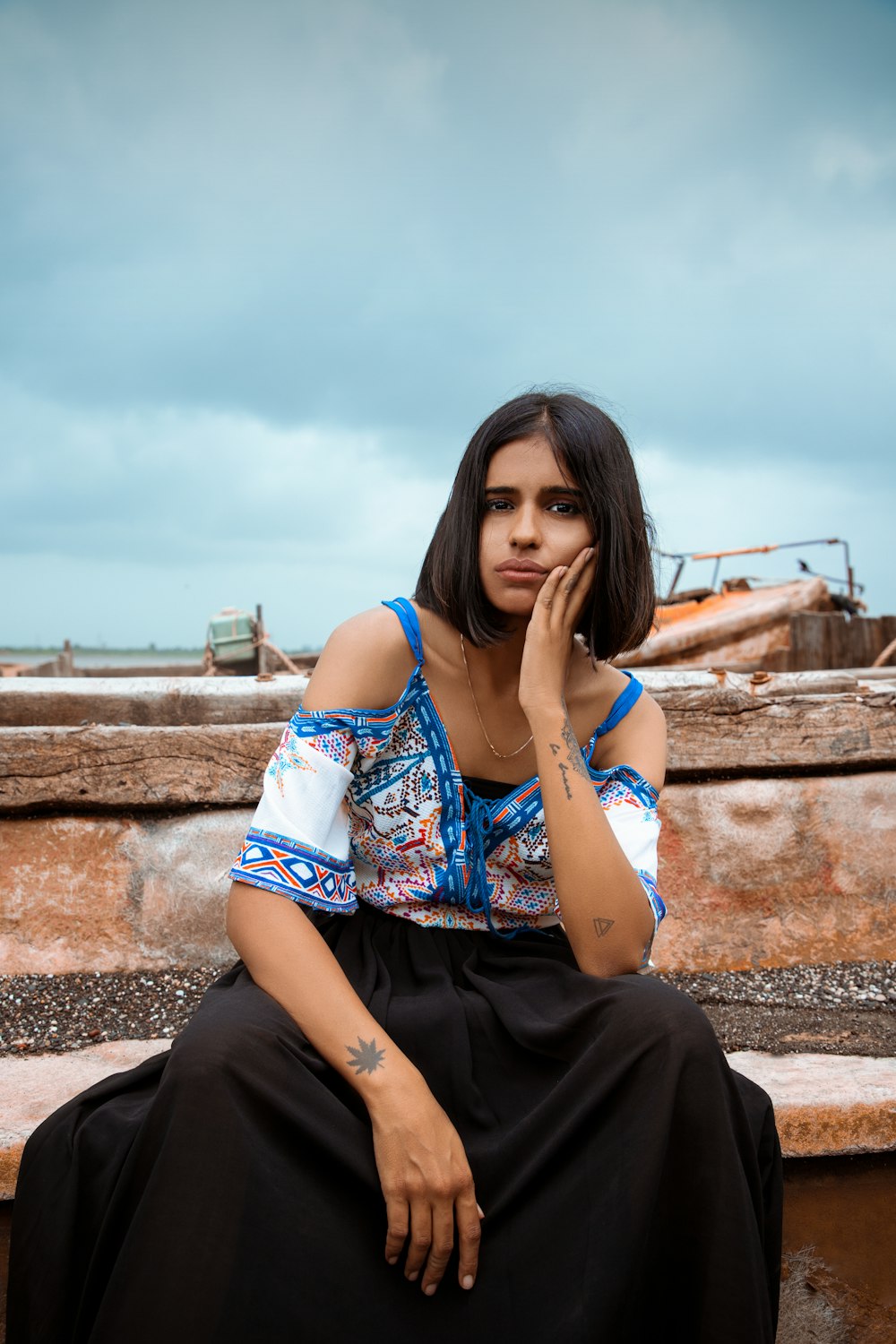 woman in blue and white floral shirt and black pants sitting on brown concrete wall during