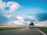 black car on road under blue sky and white clouds during daytime