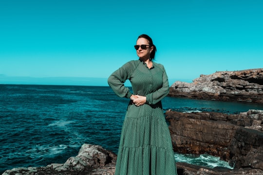 woman in green long sleeve dress standing on rock formation near sea during daytime in Hermanus South Africa