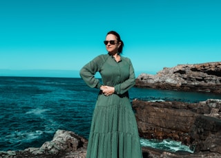 woman in green long sleeve dress standing on rock formation near sea during daytime