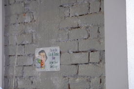 A humorous vintage-style sign is attached to a rough brick wall with faded paint. The sign features a retro illustration of a person smiling while holding a glass, accompanied by a witty caption about a 'Gin & Tonic Diet.'
