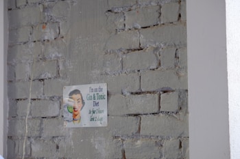 A humorous vintage-style sign is attached to a rough brick wall with faded paint. The sign features a retro illustration of a person smiling while holding a glass, accompanied by a witty caption about a 'Gin & Tonic Diet.'