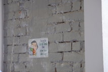 A humorous vintage-style sign is attached to a rough brick wall with faded paint. The sign features a retro illustration of a person smiling while holding a glass, accompanied by a witty caption about a 'Gin & Tonic Diet.'