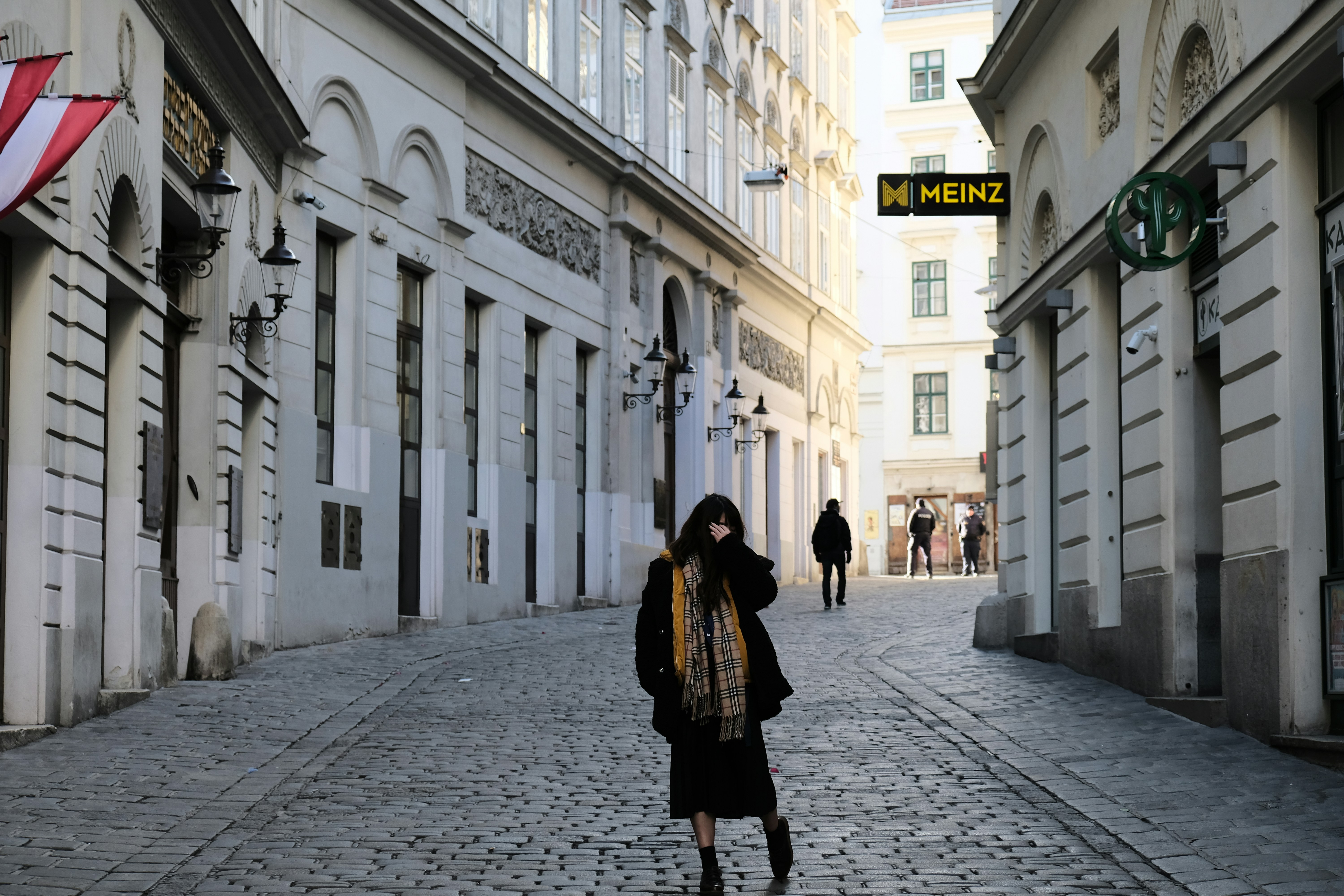 woman in black and brown coat walking on sidewalk during daytime