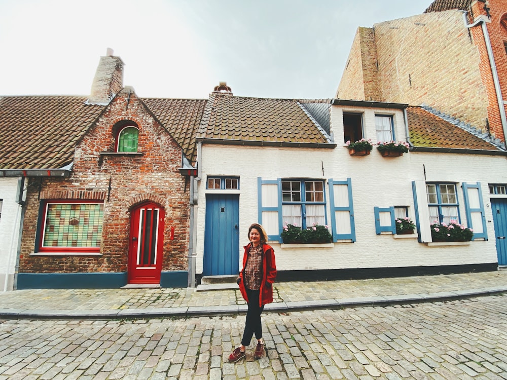 woman in red coat standing in front of white and brown concrete house during daytime