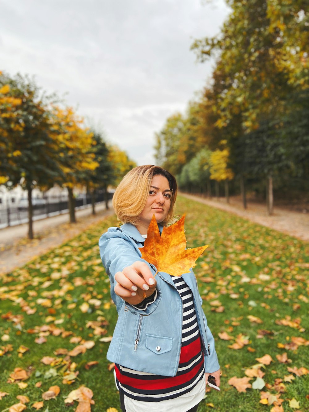 woman in blue denim jacket holding yellow maple leaf