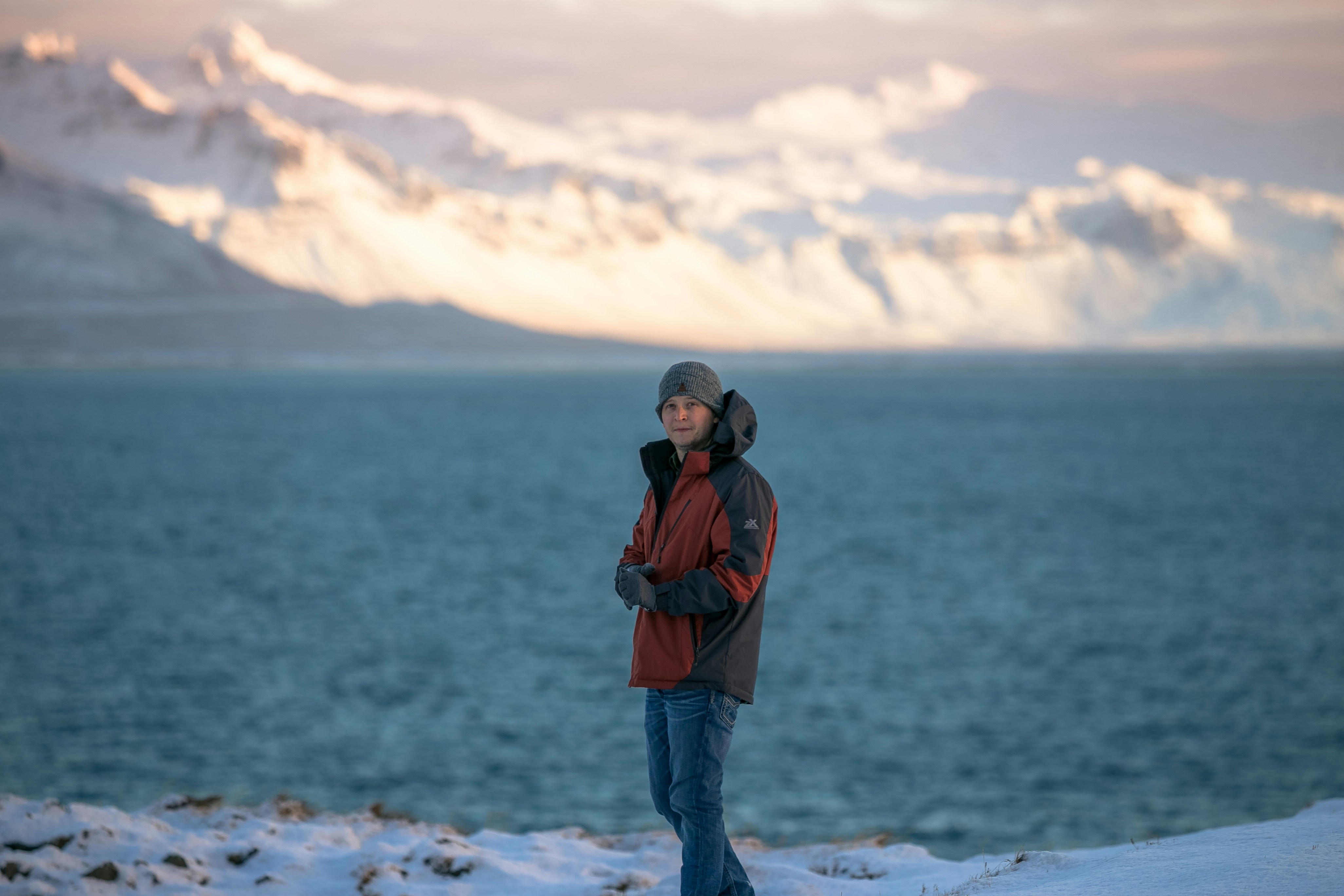 man in red jacket and blue denim jeans standing on white snow covered ground during daytime