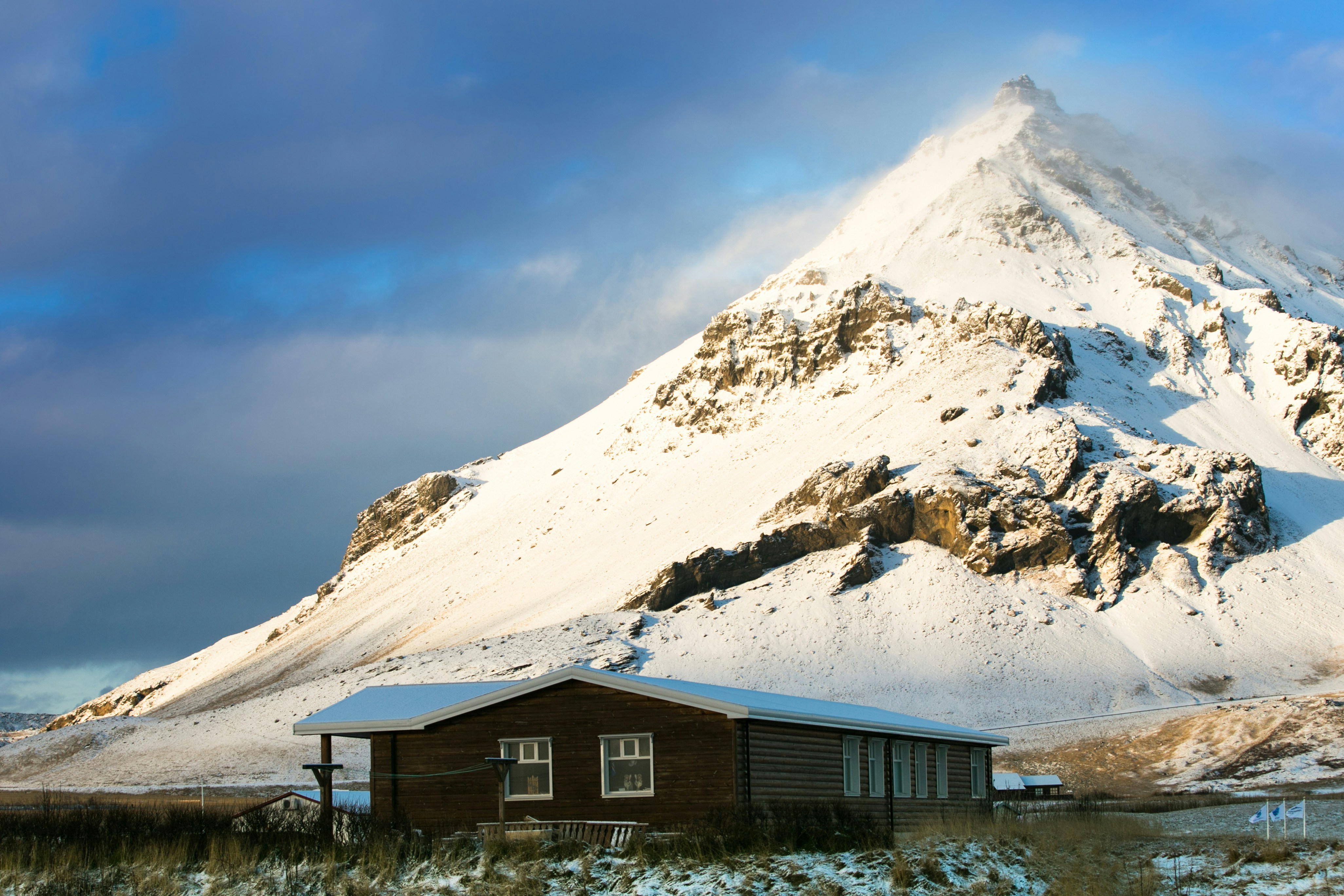 brown wooden house near snow covered mountain during daytime