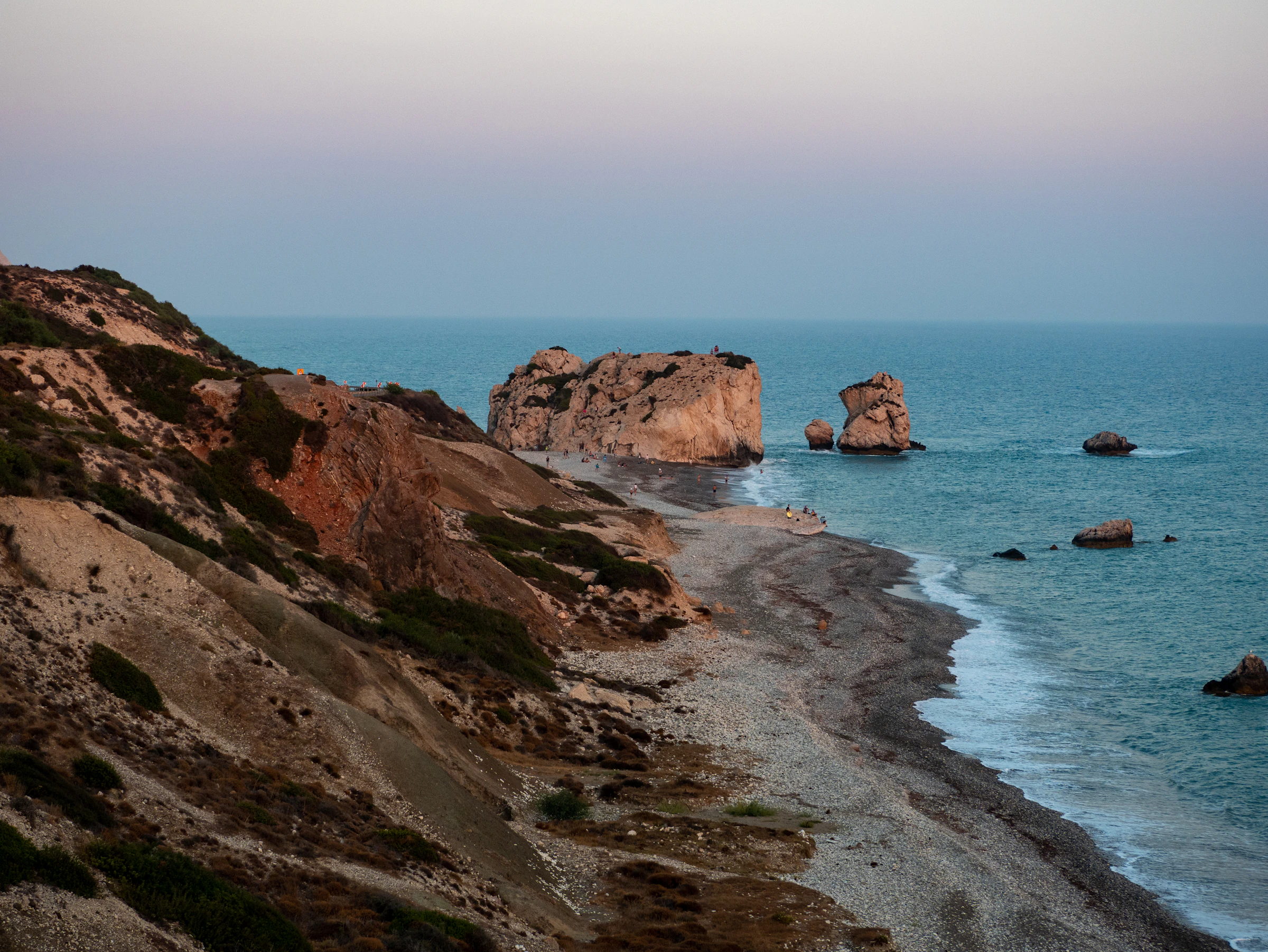 The sea stacks of Petra tou Romiou seen from the clifftop above the pebble beach at dusk