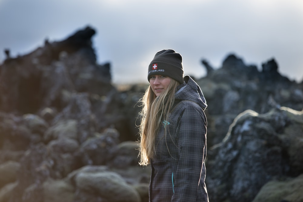woman in black and white plaid dress shirt and black cap standing on rock formation during