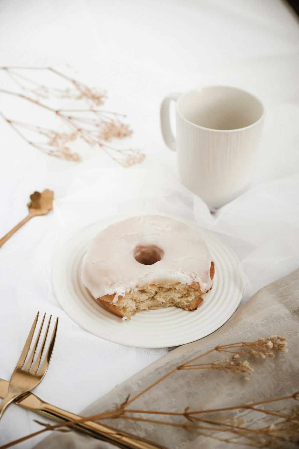 white ceramic mug beside white ceramic plate with stainless steel fork and bread knife