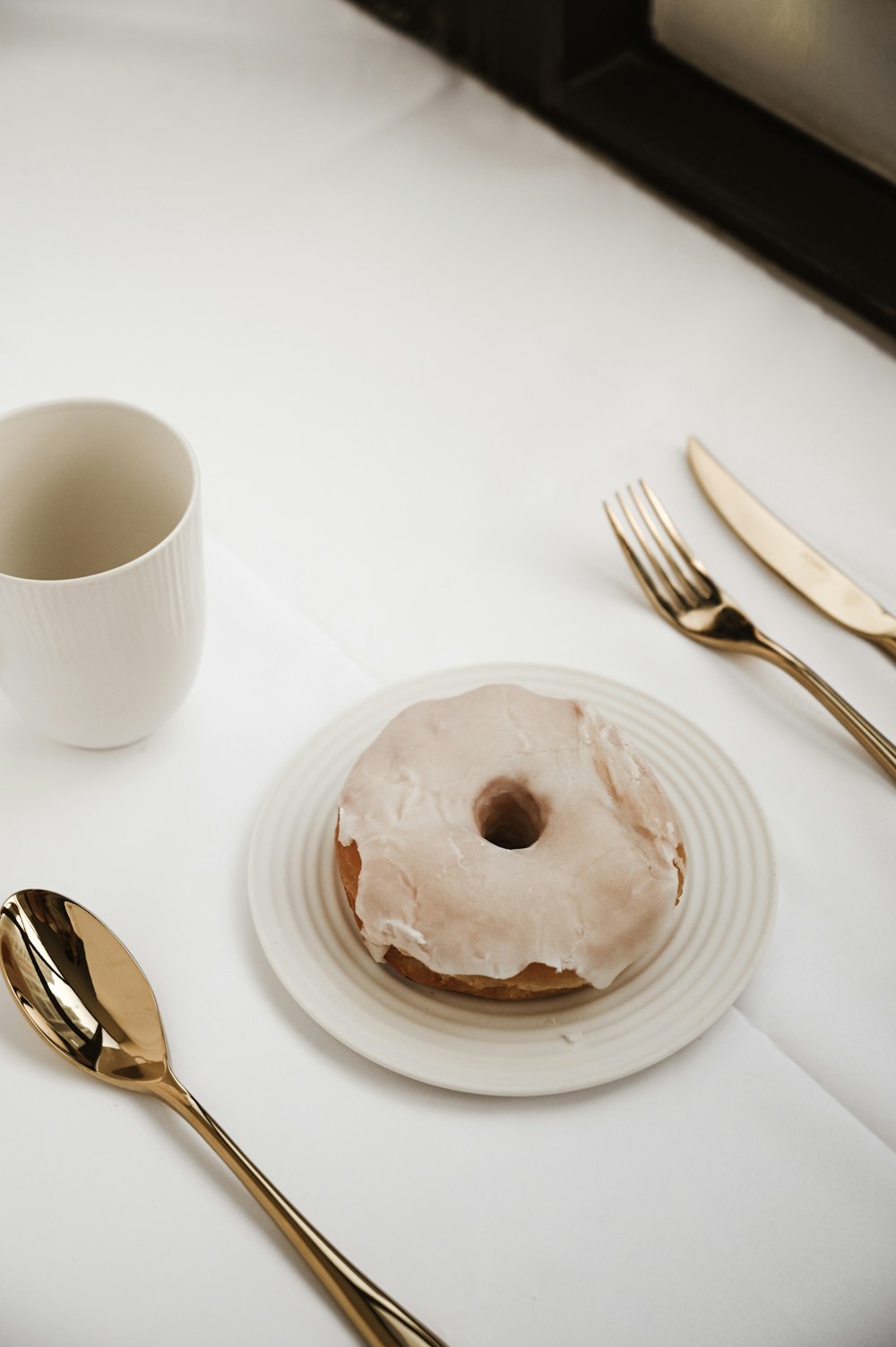 white ceramic mug beside stainless steel fork and bread knife on white ceramic round plate