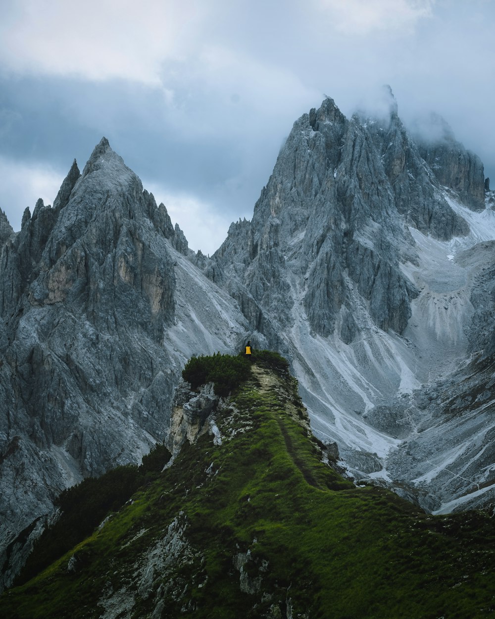 person in black jacket standing on green grass covered hill near snow covered mountain during daytime