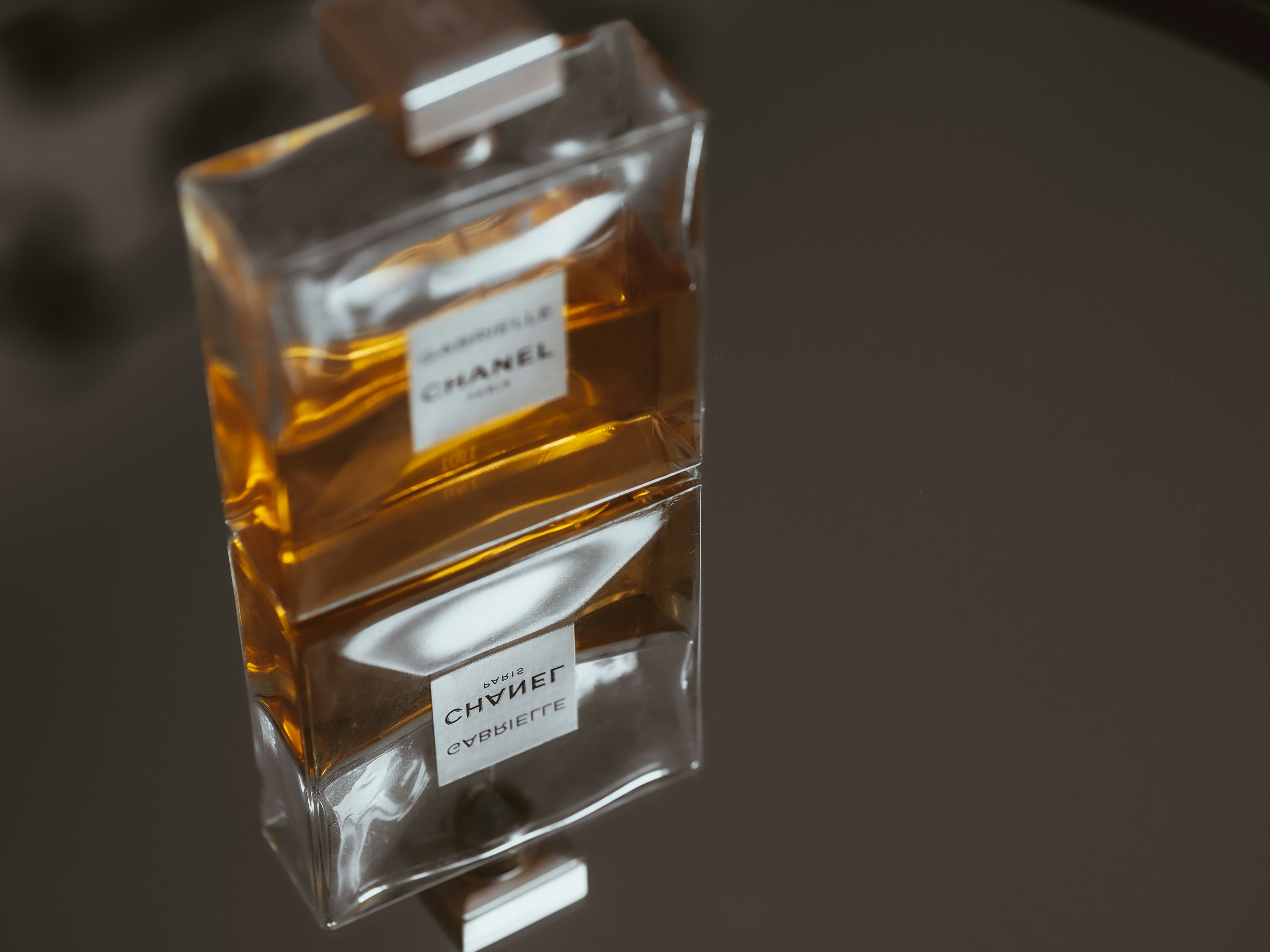 Luxury perfume flacon with crystal stopper and golden liquid on reflective dark surface, editorial lighting
