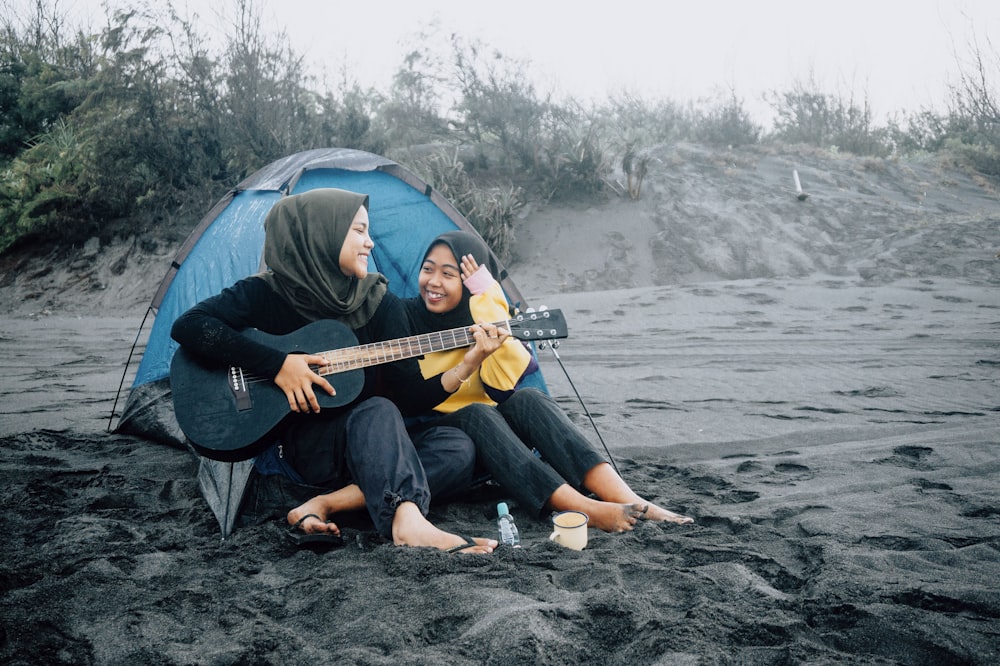 man in black shirt playing acoustic guitar sitting on blue dome tent