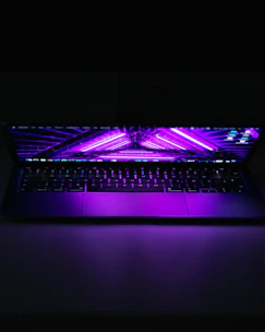 A sleek laptop screen glowing with a vibrant purple and neon website interface against a dark background