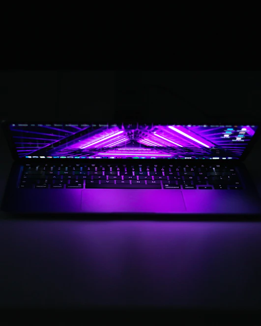 A sleek laptop screen glowing with a vibrant purple and neon website interface against a dark background