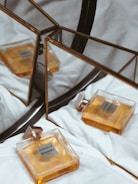A bottle of Chanel perfume is placed on a soft, white fabric surface. Its elegant design features a square glass bottle with an amber-colored fragrance, creating a luxurious and sophisticated impression. The perfume bottle is reflected in a geometric, triangular mirror, adding depth and complexity to the composition.