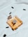 A bottle of Chanel perfume lies on a soft, white fabric. Several black capsules are scattered around it, adding a contrast to the clean and minimalist background. The perfume bottle is square-shaped with a golden hue, reflecting elegance and luxury.