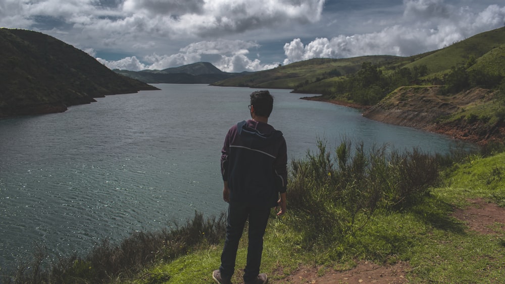 man in black jacket standing on green grass field near body of water during daytime