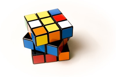 A partially solved Rubik's Cube is positioned against a plain background. The cube features a mix of colors including yellow, red, blue, orange, and white on various faces, and it appears to be slightly twisted, showing its 3D structure.