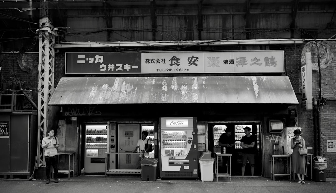 grayscale photo of man in white shirt standing near store