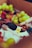 A vibrant assortment of fresh fruits and nuts arranged in a decorative manner, featuring grapes, berries, and assorted nuts accompanied by a floral garnish and a honey dipper.