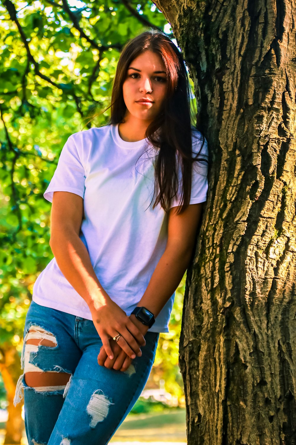woman in white crew neck t-shirt and blue denim shorts leaning on brown tree during