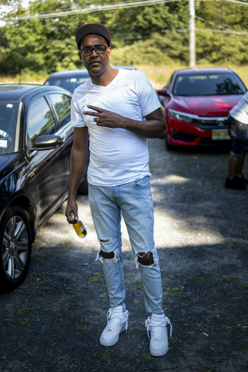 man in white crew neck t-shirt and blue denim jeans standing beside black car during