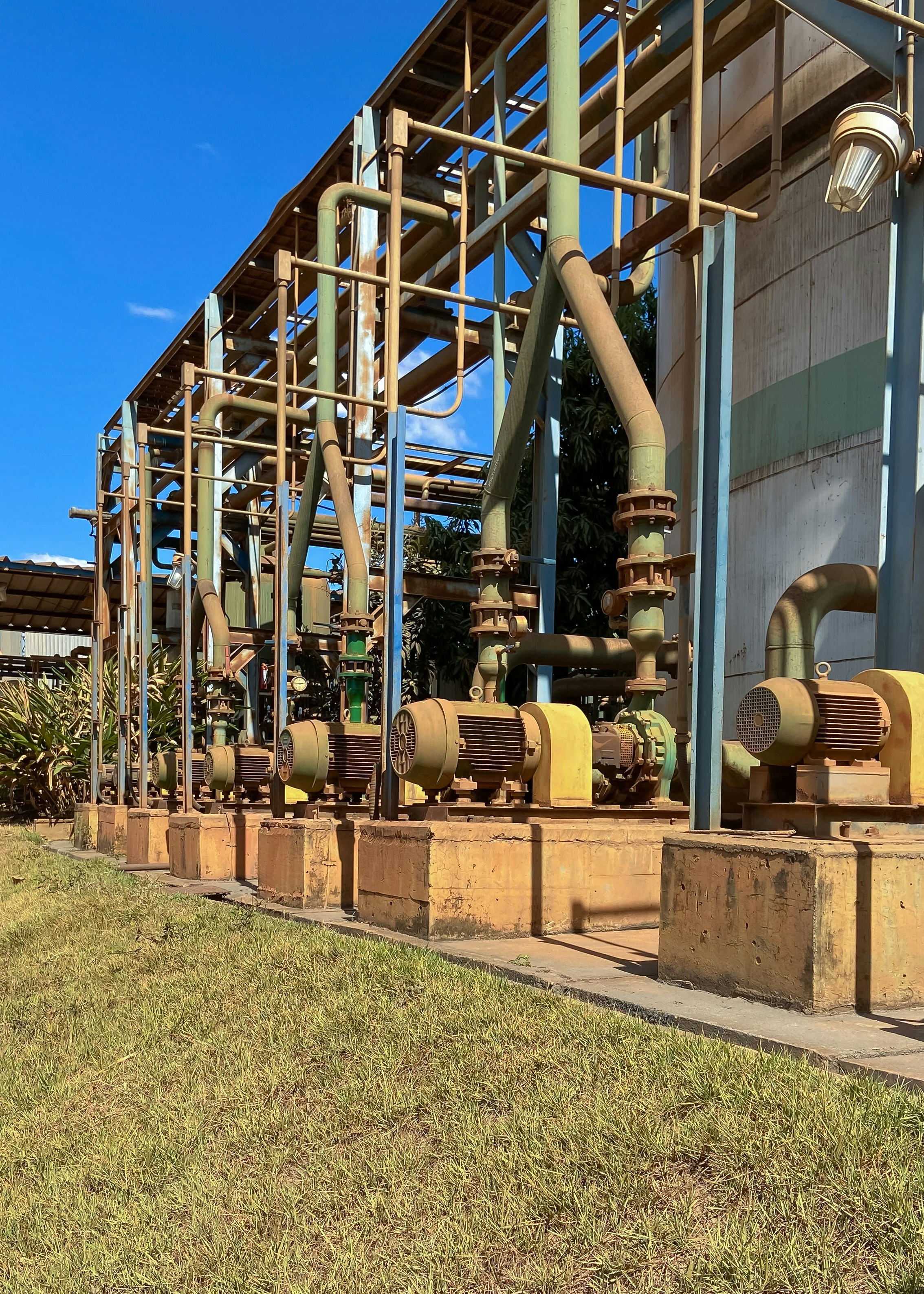 Industrial water pump and motor unit in outdoor farm setting, steel pipes, clear blue sky