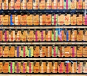 A collection of vintage train tickets displayed in rows, each ticket held in place by a metal clip. They feature various shades of orange, yellow, and blue with printed text denoting different destinations and travel information. Some tickets have bold, colorful highlights in pink and green, adding contrast to the overall muted tones.