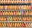 A collection of vintage train tickets displayed in rows, each ticket held in place by a metal clip. They feature various shades of orange, yellow, and blue with printed text denoting different destinations and travel information. Some tickets have bold, colorful highlights in pink and green, adding contrast to the overall muted tones.