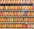 A collection of vintage train tickets displayed in rows, each ticket held in place by a metal clip. They feature various shades of orange, yellow, and blue with printed text denoting different destinations and travel information. Some tickets have bold, colorful highlights in pink and green, adding contrast to the overall muted tones.