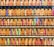 A collection of vintage train tickets displayed in rows, each ticket held in place by a metal clip. They feature various shades of orange, yellow, and blue with printed text denoting different destinations and travel information. Some tickets have bold, colorful highlights in pink and green, adding contrast to the overall muted tones.