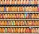 A collection of vintage train tickets displayed in rows, each ticket held in place by a metal clip. They feature various shades of orange, yellow, and blue with printed text denoting different destinations and travel information. Some tickets have bold, colorful highlights in pink and green, adding contrast to the overall muted tones.