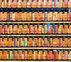 A collection of vintage train tickets displayed in rows, each ticket held in place by a metal clip. They feature various shades of orange, yellow, and blue with printed text denoting different destinations and travel information. Some tickets have bold, colorful highlights in pink and green, adding contrast to the overall muted tones.