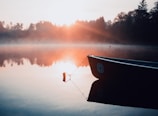 Golden sunrise over a serene mountain lake with a lone canoe.