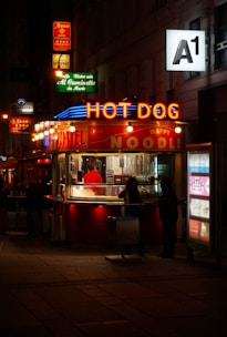 people walking on sidewalk near red and white store during nighttime